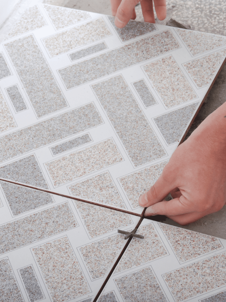 A person’s hands are measuring and marking a patterned tile with a pencil and ruler, preparing it for cutting or installation.