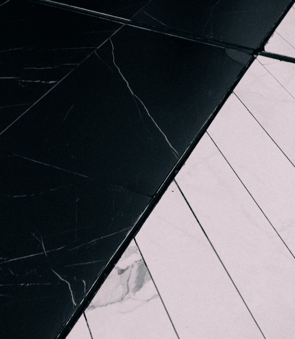 A close-up view of a floor with contrasting black and white marble tiles, each featuring subtle vein patterns. The tiles are arranged diagonally, creating a bold geometric design.