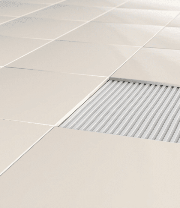 A section of beige ceramic floor tiles is missing, revealing a corrugated white surface underneath. The surrounding tiles are evenly spaced and aligned.