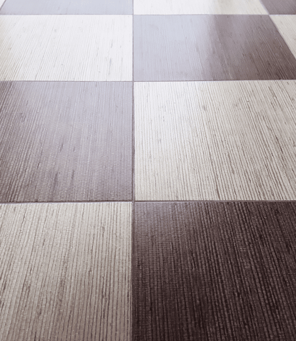 A close-up view of a checkered floor with alternating light and dark square tiles, featuring a subtle wood grain texture on each tile.
