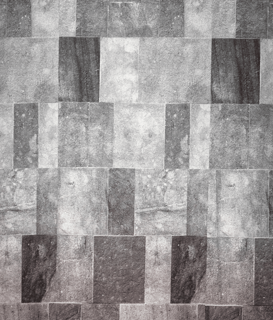 A grayscale image of a stone wall composed of rectangular tiles arranged in a repeating, staggered pattern. The tiles vary in shades of gray, with visible textures and subtle surface markings.